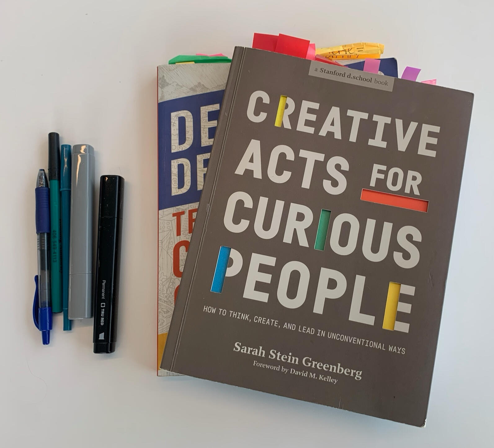 A white woman with blonde hair wearing a black shirt and brightly colored patterned scarf looks at the camera.
